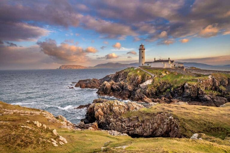 A scenic view of a lighthouse near the coast in a colorful sunset sky background