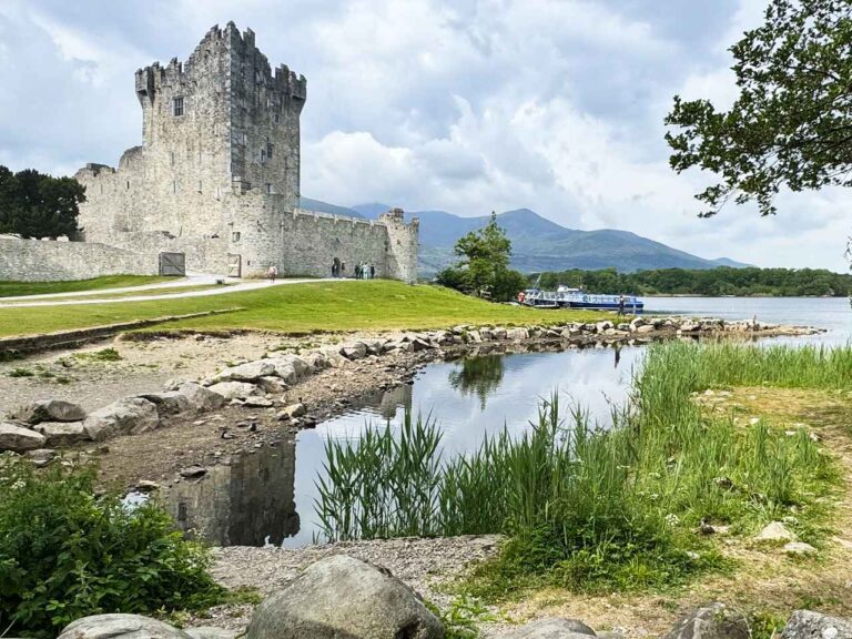 View of the Lakes of Killarney with Ross Castle, surrounded by mountains and greenery in Killarney National Park, Ireland.