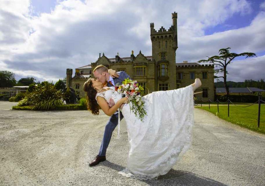 Happy bride and groom standing in front of Lough Eske Castle in Donegal, Ireland, celebrating their destination wedding in ireland